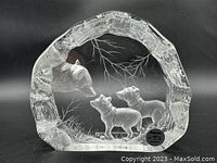 Front view of clear crystal sculpture showing wolf and two pups with engraved branches inside, with dark background for contrast.