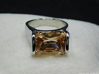 Close-up of large rectangular faceted gemstone ring, showing pink-yellow hues and silver-colored metal setting.