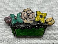 Front view of vintage silver brooch with enamel flowers and marcasite accents on green enamel flower pot base.