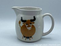 Front angle of the white ceramic pitcher showing the stylized brown and black bull illustration, handle, and pouring spout.