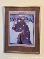 Full view of framed Vogue cover art showing a woman in a dark cloak in a snowy urban setting.