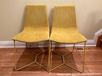 Front view of two Dijon upholstered chairs side by side against a beige wall on a wood floor