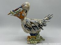 Front-left angle view of ceramic pelican sculpture, showing detailed beak with fish and yellow boots.