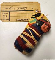 Close-up of vintage Native American baby in papoose doll with tag showing 1 1/2 cents postage stamp and hand-written recipient name