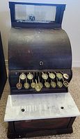 Front view of antique National Cash Register showing curved metal body, price keys, and marble base