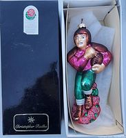 Photo showing the ornament inside the original black box displaying a vintage football player in maroon and green with a football and rose base.