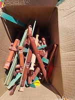 Photo of a medium box filled with numerous brown cylindrical Lincoln Log pieces and some flat green wooden planks.