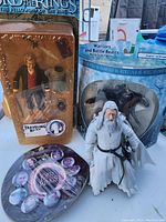 Front view showing Traveling Bilbo figure sealed in blister pack with torn plastic, boxed Aragorn on Horseback toy, loose Gandalf figurine, and Lord of the Rings button set.