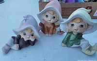 Front view of three Homco ceramic figurines of children in hats showing pastel coloring and detailed facial features.
