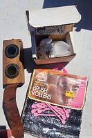Overview of lot contents showing wooden box with lenses, unopened pink spiral brush rollers, and small white plastic curler set in original box.