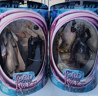 Front view of two Lord of the Rings Fellowship of the Ring action figures, Saruman and Orc Overseer, in original sealed packaging with some visible wear and dust.