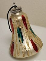 Icicle-shaped glass Christmas ornament with silver base, red and green glitter decorations, and hanging string.