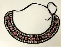 Full view of the crescent-shaped black fabric collar necklace with multicolored beaded floral pattern and black fabric ties.