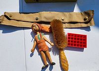 Pinocchio doll, hair brush, red Coca Cola tray, and beige belted pouch on white surface