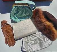 Set of two vintage purses, brown faux fur hat, and brown leather gloves displayed on a surface.