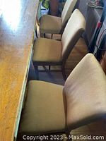 Side view of beige fabric upholstered oak dining chairs positioned next to a wooden table.