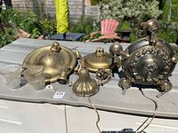 Set of three brass light fixtures arranged on outdoor surface, showing overall condition and size