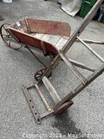 Photo of weathered wooden luggage cart with cast iron wheels, showing the seat and bottom platform, and the leather strap across underneath
