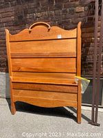 Full view of pine wood headboard with carved detail and footboard models with two hung metal rails leaning against wall.