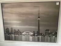 Wide view of framed black and white print showing Toronto skyline with CN Tower and illuminated buildings reflecting on water