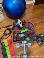 Photo showing blue yoga ball, dumbbells, ab wheel roller, foam roller stick, and massage balls arranged on floor with brown carry case.