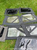 Multiple sets of Jeep Wrangler side windows laid out on grass showing fabric frames and clear and tinted plastic window panels.