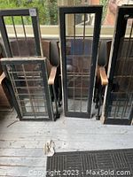 Five leaded glass windows with black wooden frames standing vertically. Visible cracked and missing glass.