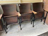 Three connected wooden theater seats on cast iron legs, side angle