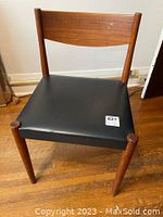 Front angled view of Mid-Century Modern teak chair with black leather seat on wood floor.