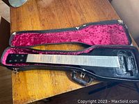 Supro lapsteel guitar body in a hard case with plush red felt lining, showing the full length of the guitar without pickups or tuners.