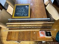 Photo showing six vintage and antique rulers (metal and wood), a small framed chalkboard with handwritten message, and a vintage Tru-Point metal pencil sharpener with original box placed on a wooden table.