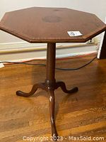 Full view of vintage walnut octagonal side table showing three-legged curved base and central pedestal column on wooden floor.