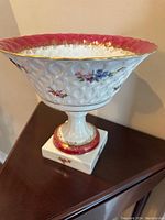 Side angle showing the white textured porcelain bowl with floral accents, pink and gold rim, and square pedestal base with matching pink and gold decoration.