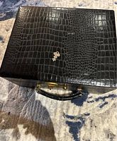 Top view of black faux alligator texture train travel case with attached handle and key resting on top