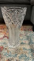 Full view of clear crystal vase showing the narrow base and wider scalloped mouth with intricate cut starburst and linear patterns.