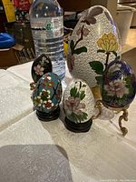 Photo showing all 5 cloisonné eggs of varying sizes with stands, placed next to a water bottle for scale.