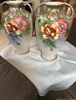 Both Nippon double-handled vases showing floral hand-painted design with gold accents, displayed on white cloth.