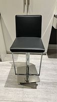 Front view of the dark graphite grey faux leather kitchen stool with chrome base, showing padded seat and backrest, chrome footrest, and square base.