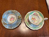 Two vintage EB Foley bone china teacups with matching saucers placed on a wooden table showcasing different floral patterns and different color schemes.