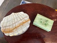 Photo showing top view of onyx shell shaped dresser box with natural color banding and green alabaster trinket box with painted flowers.
