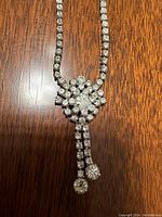 Close-up of the central floral cluster of clear rhinestones with two rhinestone dangles at the bottom on a silver tone flexible chain.