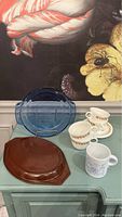 Lot arranged on blue table showing all items: 4 cups and saucers, blue glass pie plate, brown Pyrex lid, floral mug