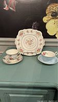 Full view of the three vintage tea set items: one dessert plate and two teacups with saucers in varied floral designs and colors.