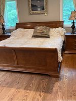 Front view of solid wood king size bed frame with headboard and footboard, cream-colored linens, decorative pillow with tiger design, wooden floor beneath
