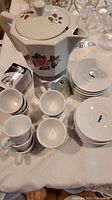 Espresso coffee set laid out on table including ceramic top espresso pot, 12 white espresso cups and saucers, and Recafimil Nespresso capsule.