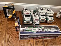 Overview photo of five Hess toy trucks and Cat 950 H loader in box on wooden floor.