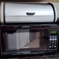 Front view of the black Sunbeam microwave with keypad and digital display on the right and the cream tin breadbox with black trim sitting on top.