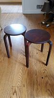 Two dark wood stools with round tops and curved legs, placed on a hardwood floor, showing overall view of the pair.
