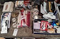 Top-down image showing assorted pantyhose packages, multiple candles held in a Ziploc bag, metal candle holders, a box with picture frames, watches, and other small items.