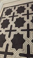 Photo showing geometric beige design pattern on a black synthetic pile rug surface, close-up of rug detail.